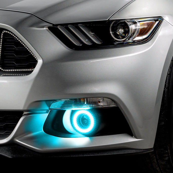 Close-up on the front bumper of a silver Ford Mustang equipped with cyan fog light halos.