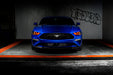 Straight front view of a blue Ford Mustang with red headlight halos and DRLs.