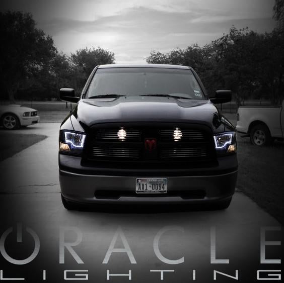 Front end of a black Dodge Ram with white LED headlight halo rings installed.