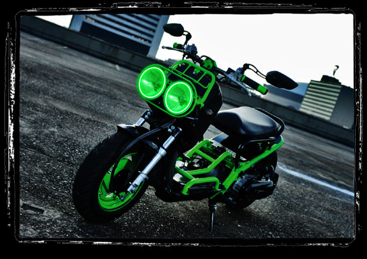 Three quarters view of a Honda Ruckus with green LED headlight halo rings installed.