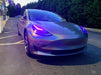 Three quarters view of a Tesla Model 3 with pink headlight DRLs.