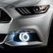 Close-up on the front bumper of a silver Ford Mustang equipped with white fog light halos.